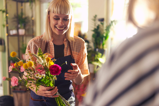 A cheerful flower shop owner prepares a flower arrangement for a customer
