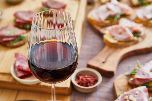 Red wine in a glass, sandwiches for social gathering or birthday event, with fresh green salad, ham, cheese, mayo, mustard, tomato, cucumber, pesto, cottage cheese, cream cheese, avocado, Spanish onion with healthy seasoning, herbs and spices, served on a wooden home table, representing a wellbeing and a healthy lifestyle, food indulgence and joy, an image with a copy space
