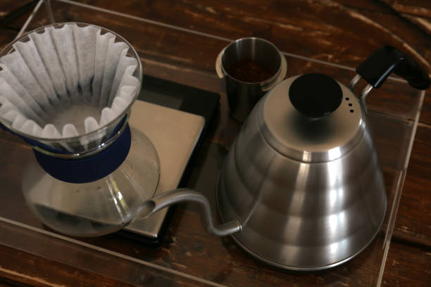 istock Cup with coffee, wave dripper and kettle on wooden table in cafe 1487849010