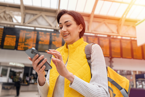 woman with backpack and holding smartphone while at the train station and the train is arriving., Enjoying travel concept