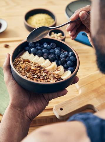 A healthy oatmeal for breakfast, with fresh organic fruit, nuts and grains, at a wooden table in a modern white kitchen, representing a healthy lifestyle and wellbeing, an image with a copy space