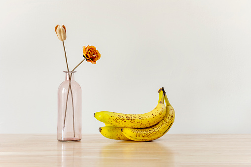 Decorative vase and a lot of ripe bananas on light wooden table