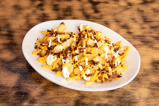 A white china tray with a large serving of French fries topped with various types of melted cheese with bits of slightly charred fried bacon
