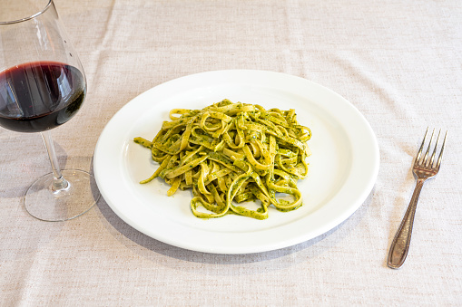 typical italian fettuccine recipe with pesto sauce on table with linen tablecloth, fork and glass of red wine