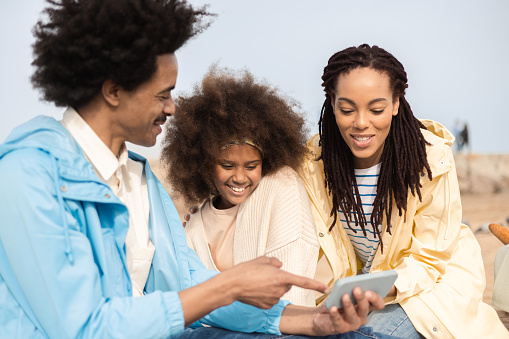 Portrait of a happy African American family enjoying a picnic on the beach and using smartphone