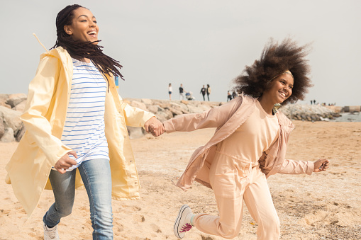 Portrait of a happy African American woman and her teenage daughter running and having fun on the beach