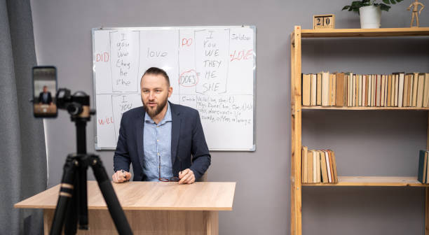 istock Male English teacher having video conference chat with students and class group, using smartphone. Millennial man talking to webcam, explaining rules in English lesson. Online Education 1487860019