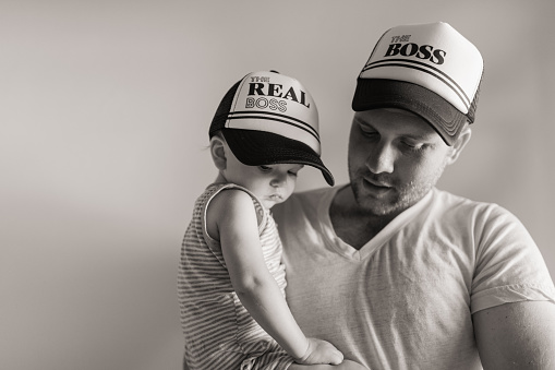 A 31-Year-Old Father Holding His 1-Year-Old Son While They Wear Matching Baseball Caps for Father's Day That Say 