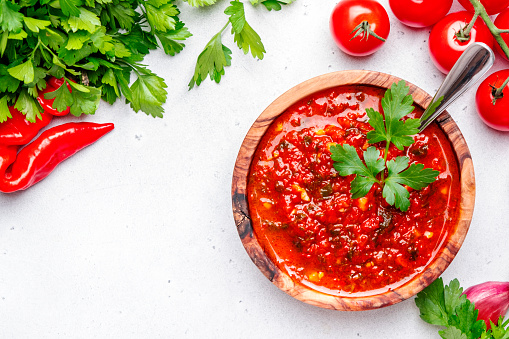 Spicy tomato pepper sauce with hot chili peppers, garlic and herbs on white kitchen table background, top view