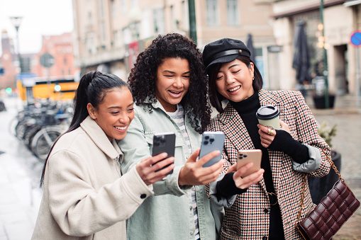 Close up of Three young women using their phones on a city street