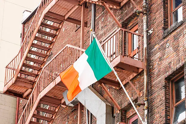 An old red brick building with metal fire escape flying an Irish flag