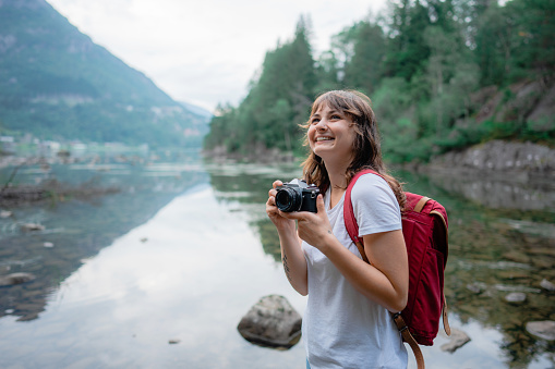 Young Caucasian woman standing near the lake and  photographing it with analog camera