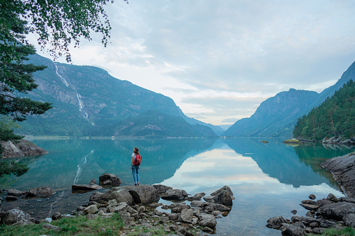 Young Caucasian woman in white t-shirt and with backpack standing on the background of  the lake in Norway