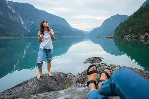 POV of man sitting and looking at  woman standing near the lake in Norway