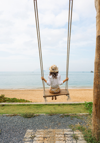 Young elegant woman on the swing on idyllic tropical beach