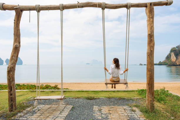 Young elegant woman on the swing on idyllic tropical beach