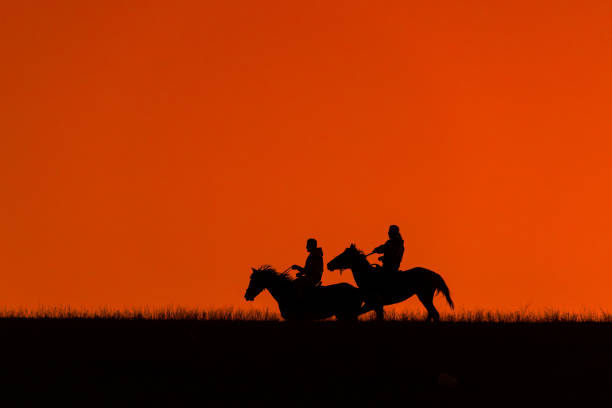 Almaty, Kazakhstan, 05.05. 2023. Silhouettes of two riders against the backdrop of a spring sunset in the evening