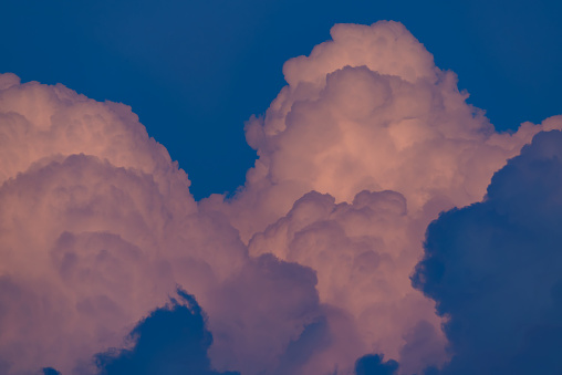 Beautiful cloudscape view of huge cumulus fluffy clouds growing over a blue sky in the evening, with warm sun light on them. Weather conditions and climate detail background. Above the clouds view.