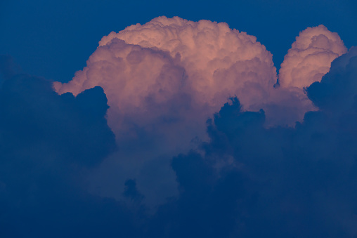 Beautiful cloudscape view of huge cumulus fluffy clouds growing over a blue sky in the evening, with warm sun light on them. Weather conditions and climate detail background. Above the clouds view.