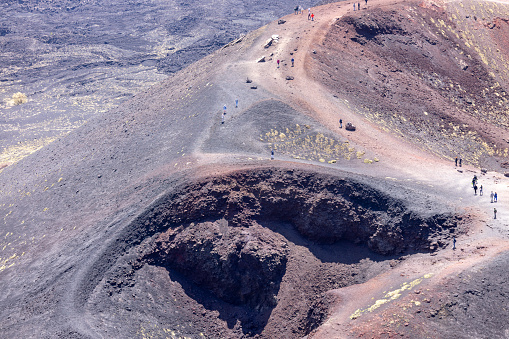 Mount Etna, Sicily, Italy - April 27, 2023: People walking above the Crater Silvestri on the slope of volcano Mount Etna. It is active stratovolcano, tallest and largest volcanic cone in Europe