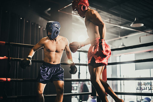 Asian and Caucasian boxer unleash knee attack in fierce boxing training session, delivering knee strike to sparring trainer, showcasing boxing technique and skill. Impetus