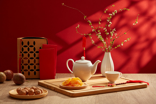 A tea set placed on wooden tray with dried candy and flower pot. Red-themed background for new year concept. Chinese new year