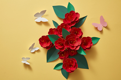 A pile of red paper flowers with few butterflies in many colors. 3d paper flowers isolated on yellow background, decorative design elements. Flat lay, top view