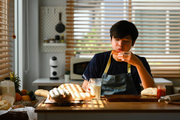 istock Handsome young asian man eating a slice of bread with jam for breakfast in kitchen. 1487906792