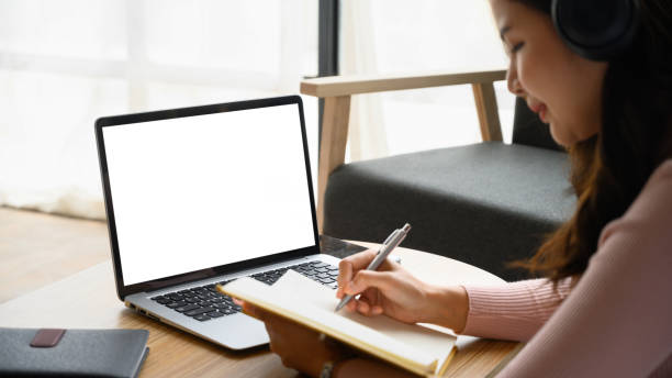 istock Concentrated young woman having distance learning online virtual class on laptop and making notes on notebook. 1487907385