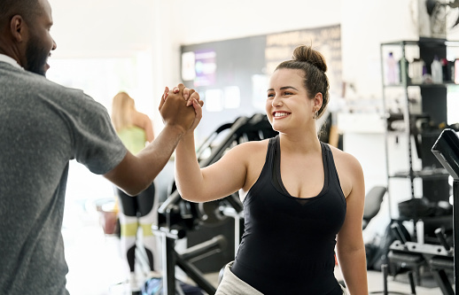 Smiling young woman giving a high five to her fitness trainer at the gym after workout session