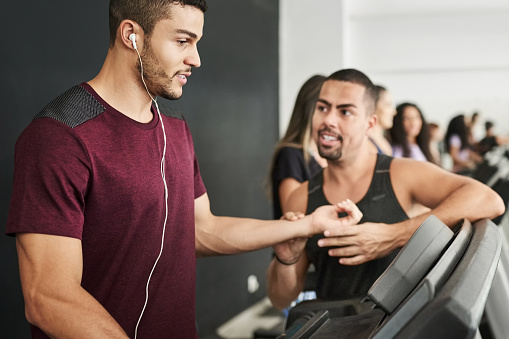 Personal trainer checking the pulse of young male walking on a treadmill in gym