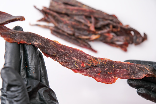 Snack of dried red meat in the hands of a chef in black gloves. Traditional snack for beer. Close-up.