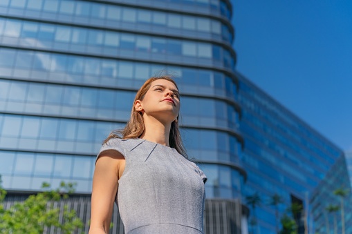 Low angle portrait shot of a confident and successful young businesswoman in the city with modern corporate skyscrapers in background. Female leadership. Determination to success. Businesswoman on the move. Connecting business relationship across the city.