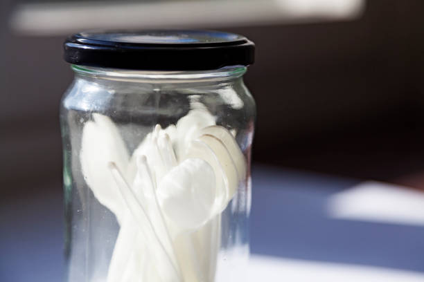 a glass jar with black lid with small white plastic spoons stands in the windowsill - plastic jars sweden bildbanksfoton och bilder