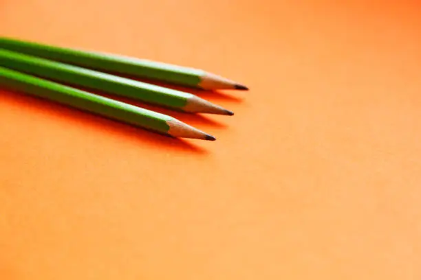 three green pencils lying on an orange background