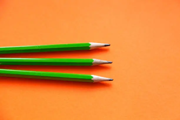 three green pencils on an orange background
