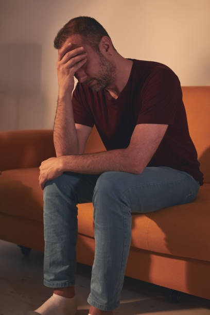 istock Man with headache sitting on a sofa at home. 1487914193