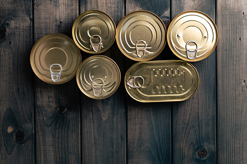 Closed food tin cans on dark background, copy space