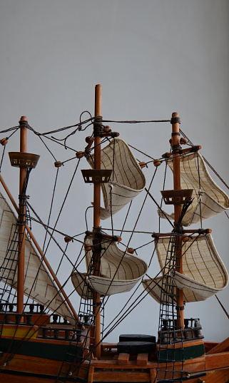 Wooden sailboat scale model with fabric sails and thread ropes closeup on white background