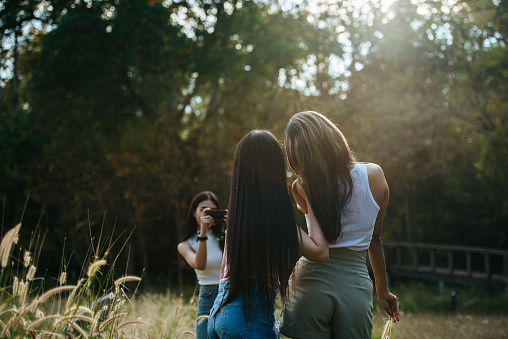 Back view of Cheerful group of happy women friends take photography with digital camera, Young woman take photos beautiful girl friends enjoy to pose in park with sunlight, selective focus