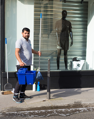 Lyon France: A window washer looks at the camera in front of a men’s clothing boutique in early morning.