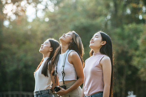 Group of Young pretty woman with girl friends standing with feeling refreshed in beautiful nature of forest, They are smile and breathed the fresh air happily.