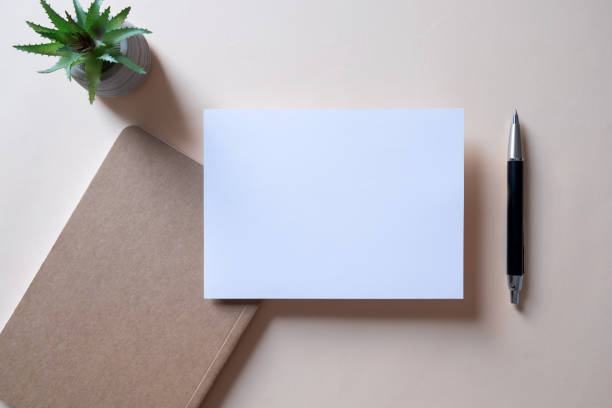 istock Workspace with note book, blank greeting card, cactus and pen on beige background. 1487928579