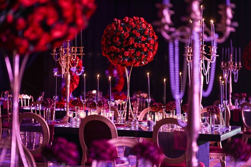 A beautiful bouquet of red roses on a wedding table surrounded by glowing candles.