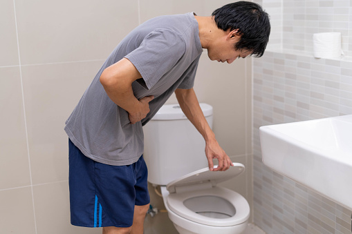 Un hombre de pie tiene diarrea y alimentos severamente tóxicos. Hombre toca vientre en el baño. Dolor abdominal, Diarrea, Concepto de cáncer de colon photo