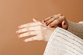 Woman applying cream on hands at brown background