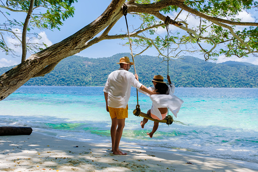 Couple playing at a rope swing on the beach of Ko Ra Wi Island Southern Thailand, tropical white sandy beach with turqouse colored ocean at Tarutao National Park, Koh Rawi, Tambon Ko Tarutao