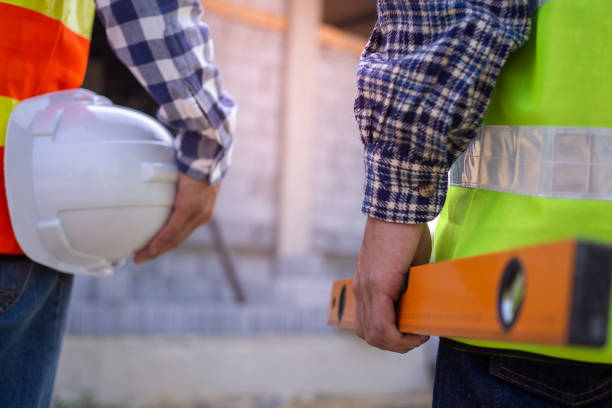 istock Professional engineers and builders in work clothes with tools and holding white helmets while standing outside the construction site. 1487951526
