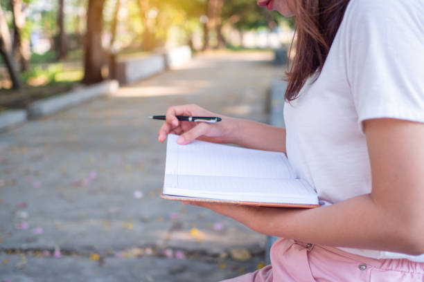 istock a young woman's hand by writing a pen on a park notebook in the evening. 1487951813