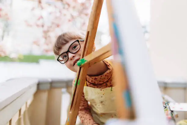 The girl with Down syndrome hiding at the easel in the art-therapy session